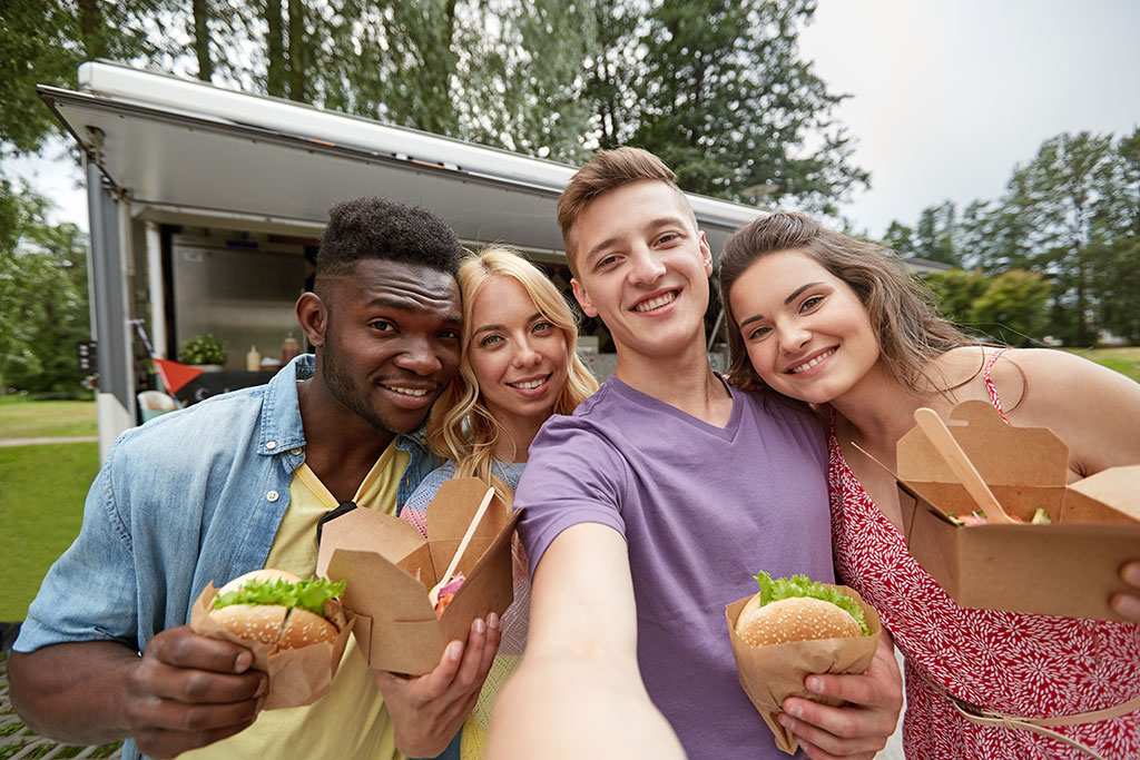 A happy group of four, two men and two women, taking a group selfie with food taking selfie at food truck.